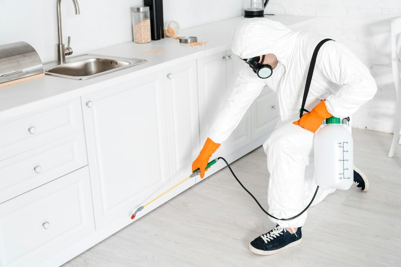 exterminator holding toxic equipment near kitchen cabinet