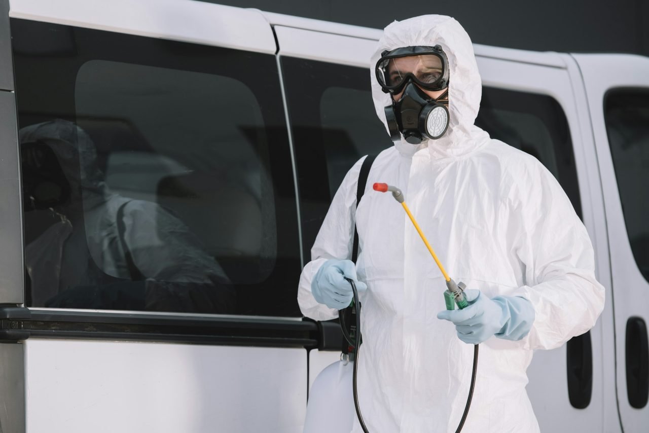 pest control worker in uniform standing near car on street and holding sprayer