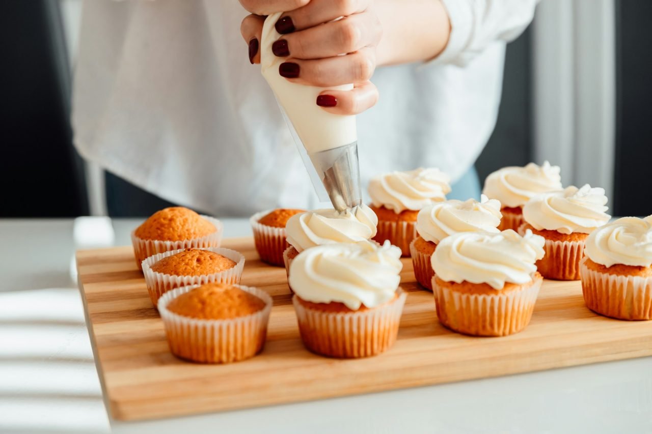 Woman decorates freshly baked cupcakes with cream