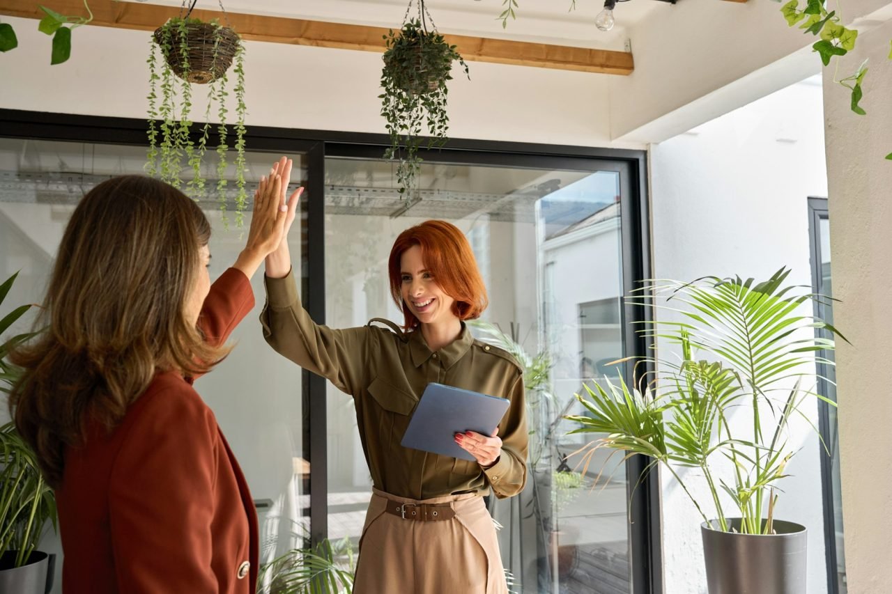 Two happy women celebrating business success giving high five in office.