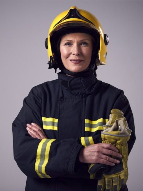 Studio Portrait Of Smiling Mature Female Firefighter Against Plain Background