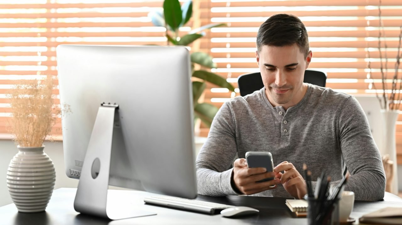 Attractive man sitting at home office and using smart phone.