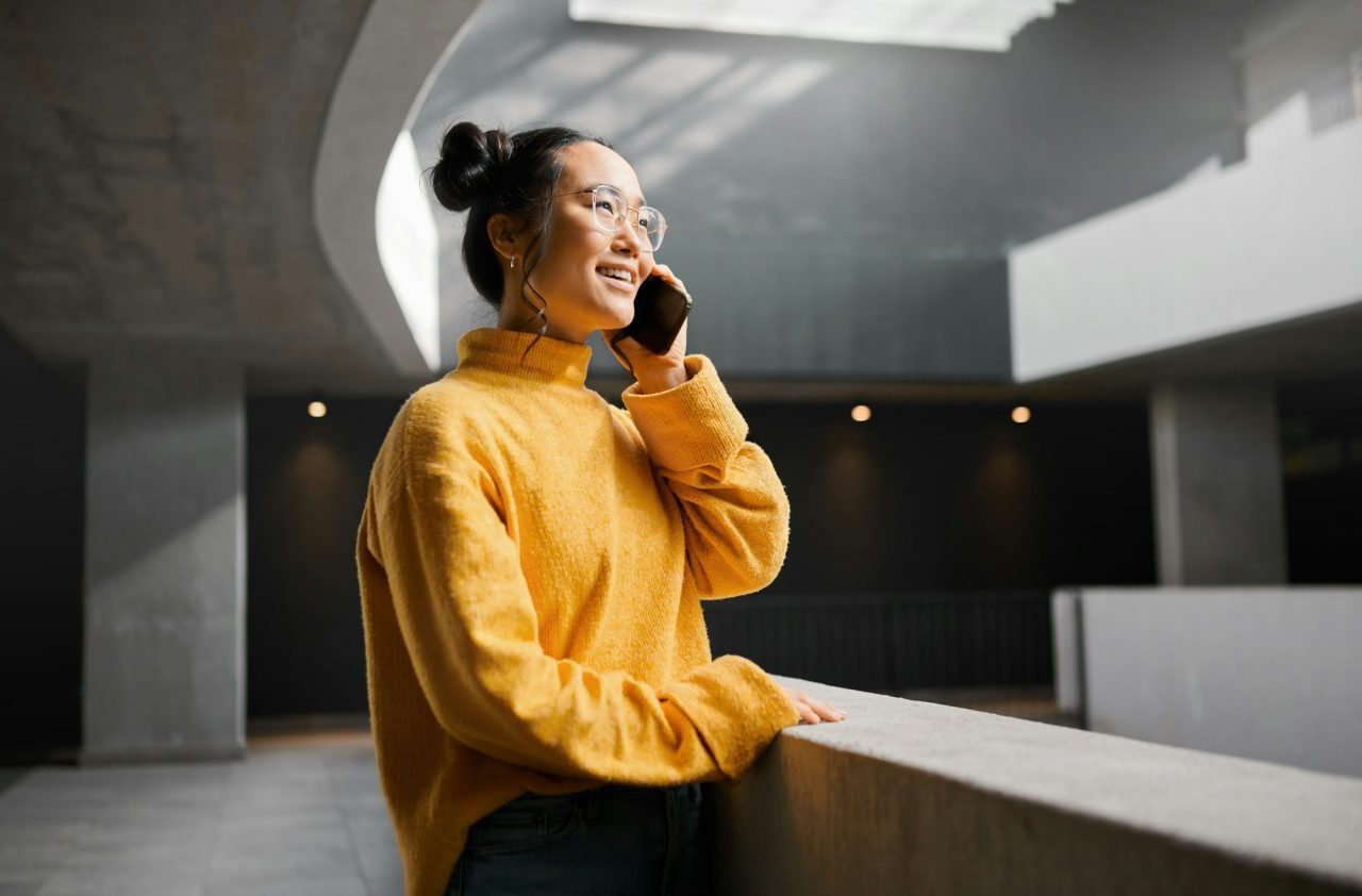 Phone call, networking and mockup with an asian woman talking while standing in a hallway. Mobile,